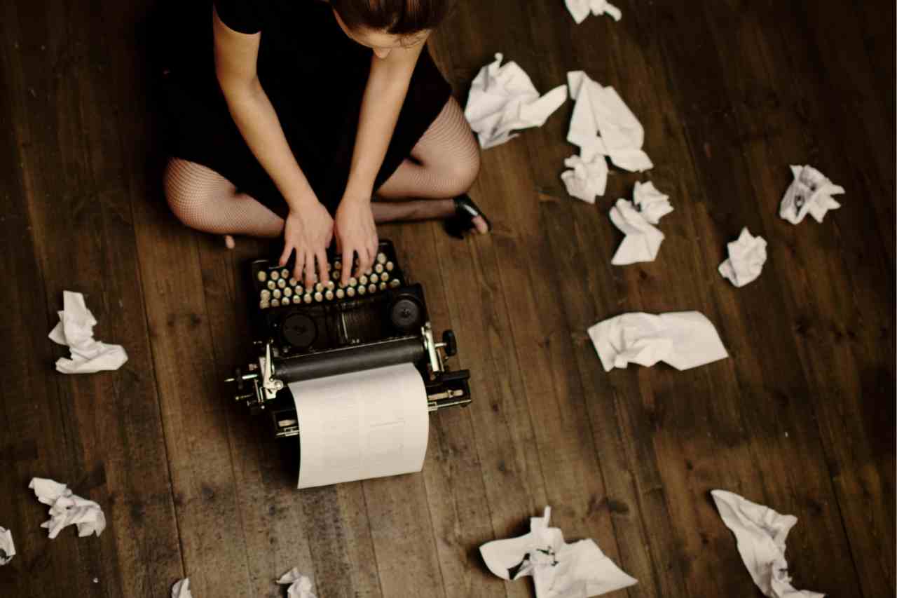 Woman on floor typing on a typewriter with crumbled paper around her